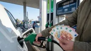 Persona fa rifornimento a un'auto tenendo in mano banconote in euro