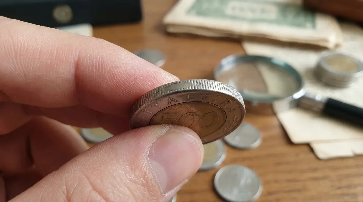 Una mano tiene una vecchia moneta da 500 lire con il bordo visibile