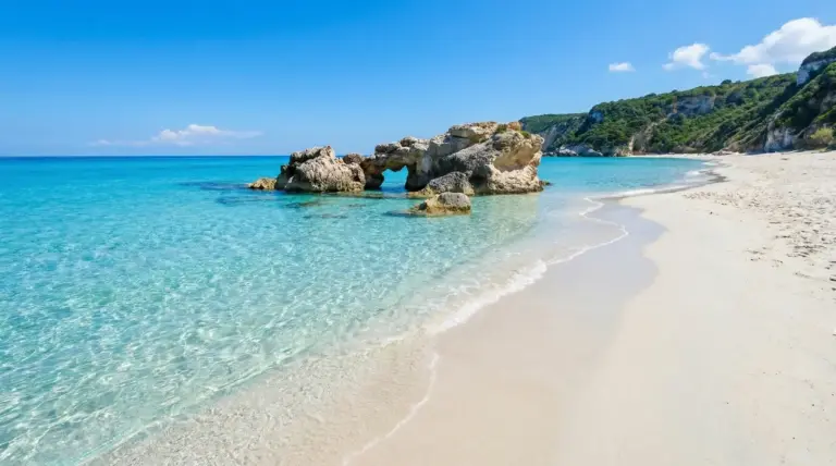 Spiaggia sabbiosa con mare cristallino e formazioni rocciose in riva, sotto un cielo sereno