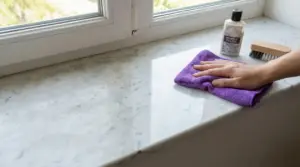 Mano che lucida un davanzale in marmo con un panno viola vicino a prodotti per la pulizia